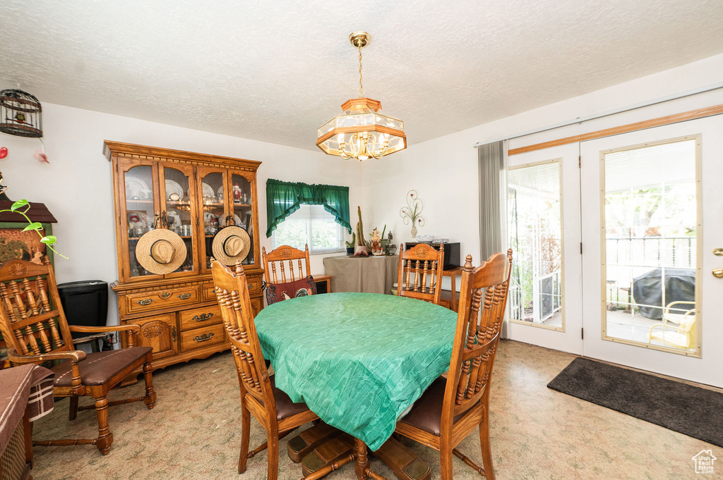 Dining space with light carpet, a wealth of natural light, an inviting chandelier, and a textured ceiling