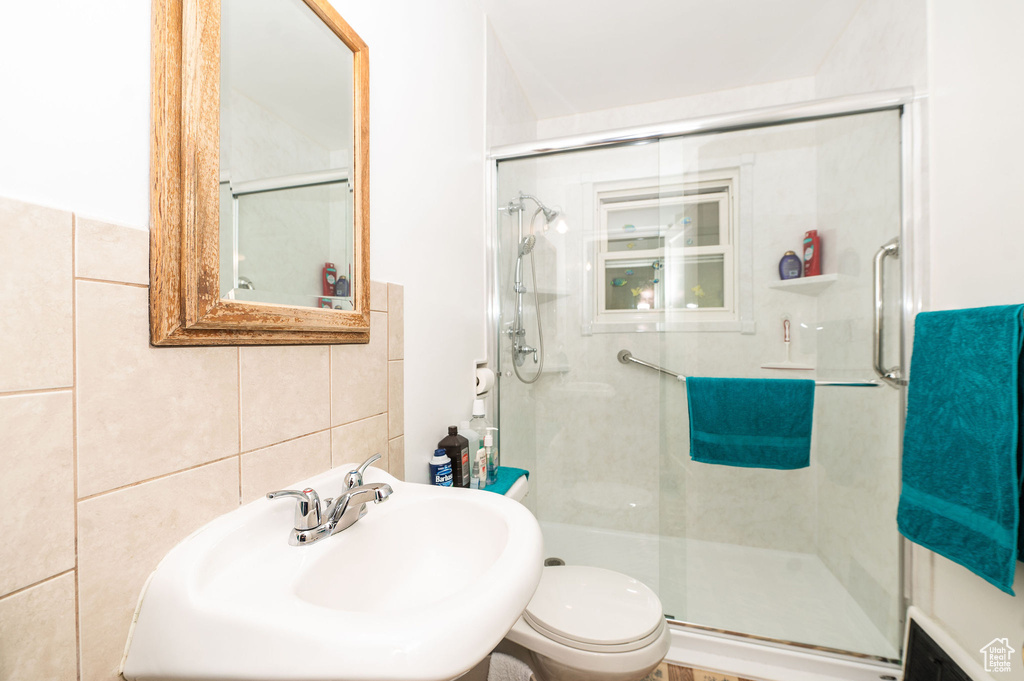 Bathroom featuring an enclosed shower, sink, toilet, and tile walls