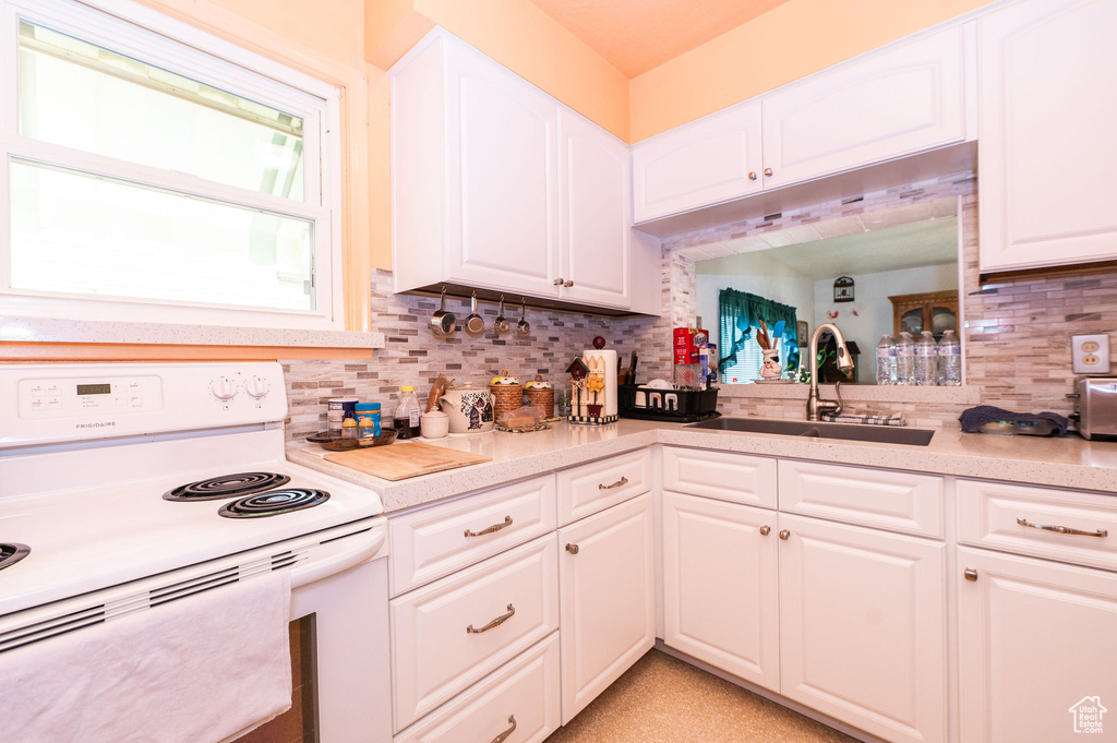 Kitchen featuring tasteful backsplash, white electric range oven, white cabinets, and sink