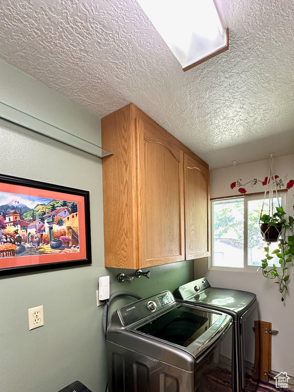 Washroom featuring washer and dryer, cabinets, a skylight, and a textured ceiling