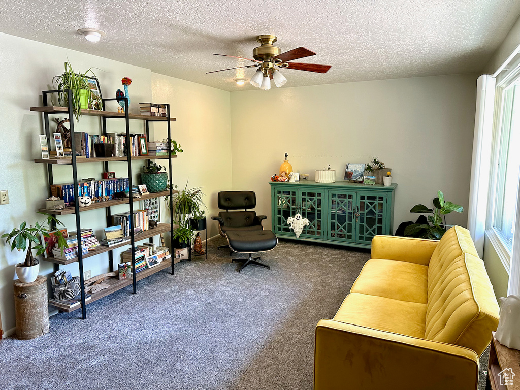 Living area with ceiling fan, a textured ceiling, and dark colored carpet