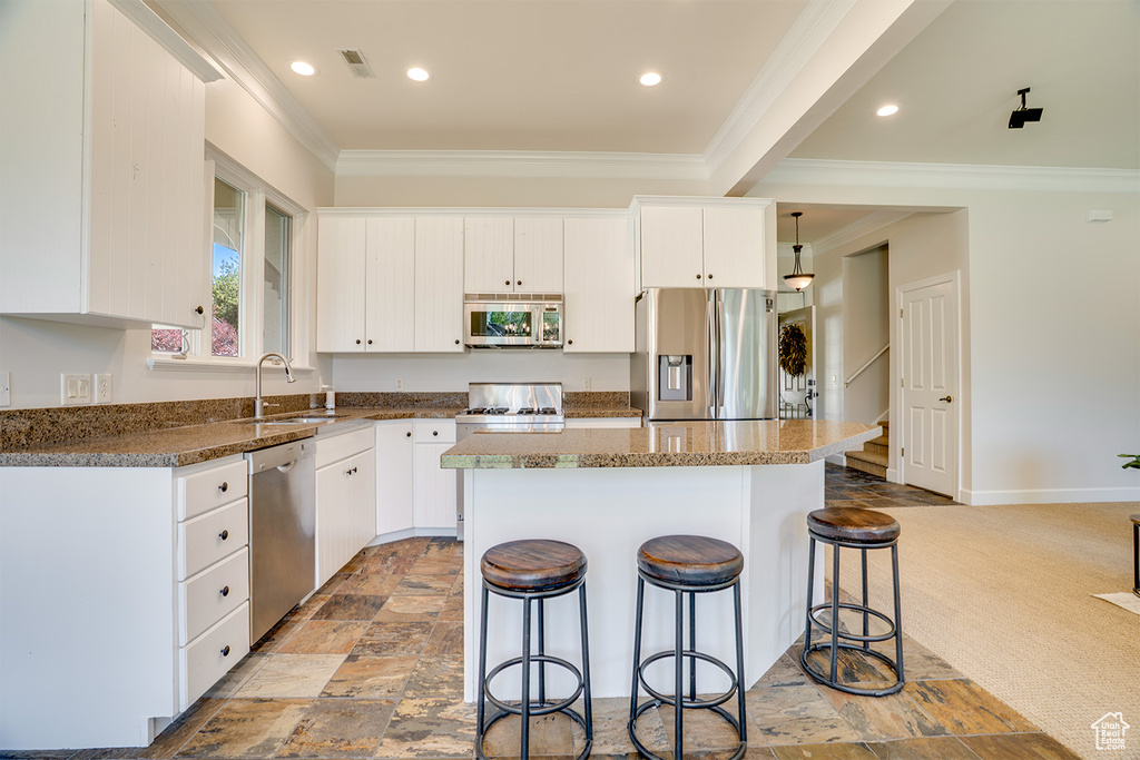 Kitchen featuring appliances with stainless steel finishes, a sink, ornamental molding, a center island, and a kitchen breakfast bar