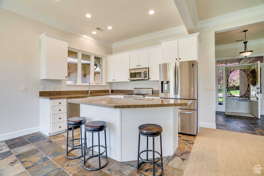 Kitchen with appliances with stainless steel finishes, crown molding, stone tile floors, a breakfast bar area, and baseboards