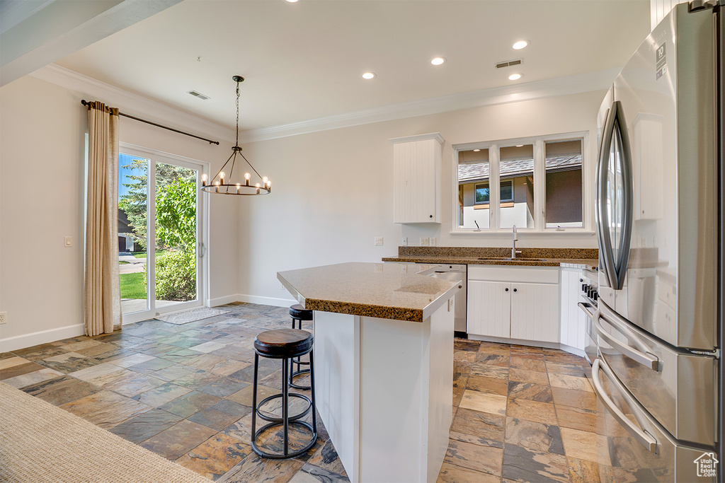 Kitchen featuring stainless steel appliances, stone tile floors, a sink, ornamental molding, and baseboards