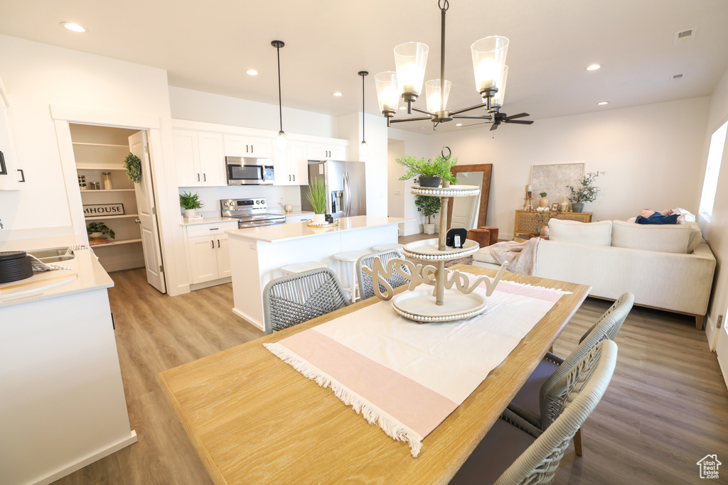 Dining area featuring ceiling fan with notable chandelier, sink, and light hardwood / wood-style flooring