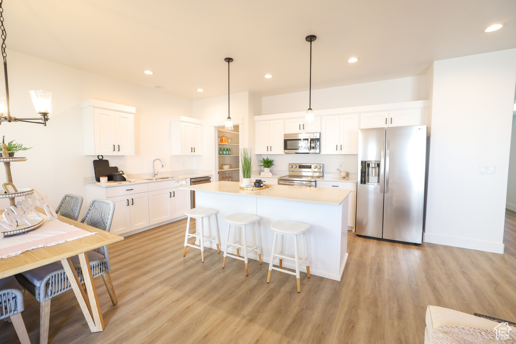 Kitchen featuring appliances with stainless steel finishes, light wood-type flooring, decorative light fixtures, and white cabinets