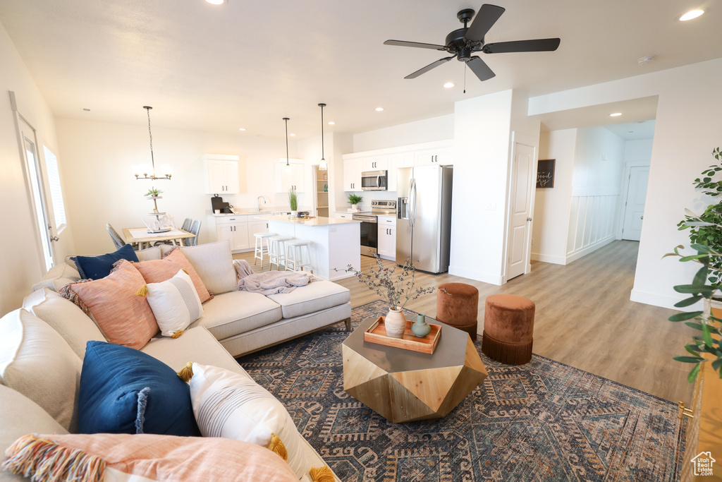 Living room with ceiling fan with notable chandelier and light wood-type flooring