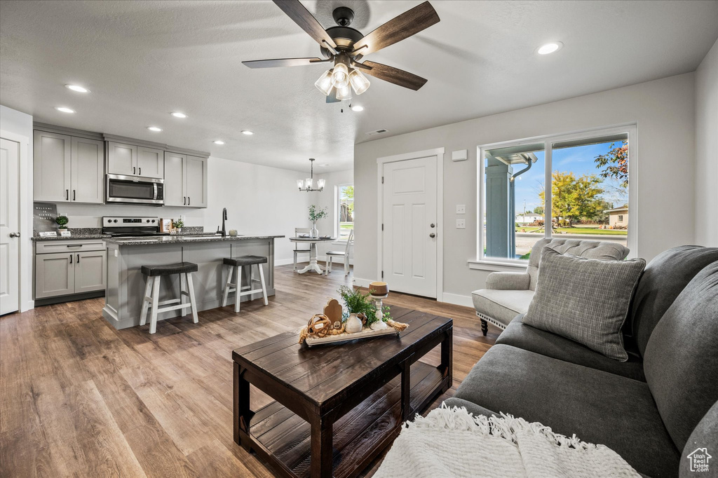 Living room featuring ceiling fan with notable chandelier, sink, and light wood-type flooring