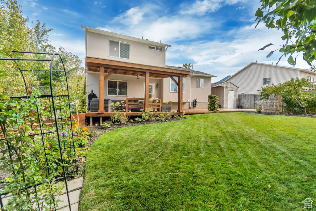 Rear view of house with ceiling fan, a yard, a wooden deck, and a shed