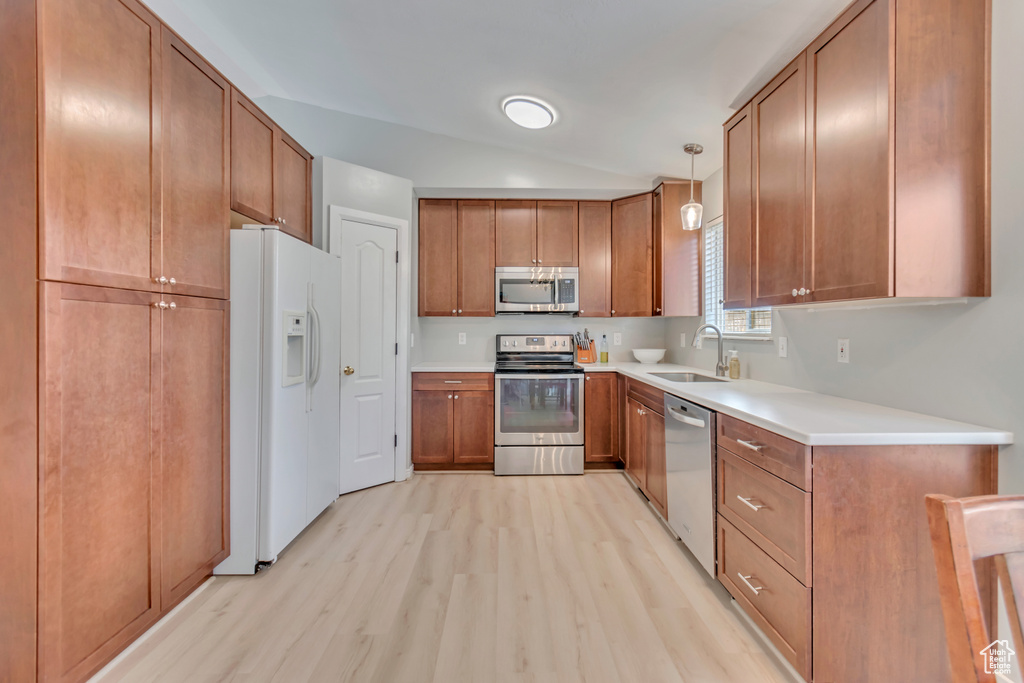 Kitchen with lofted ceiling, hanging light fixtures, sink, appliances with stainless steel finishes, and light wood-type flooring