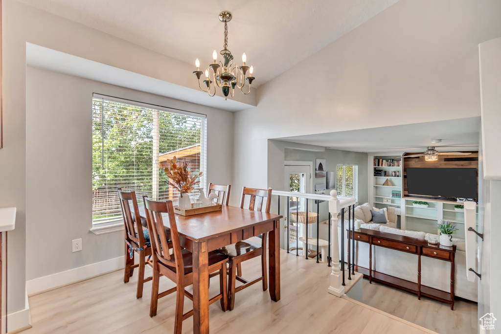 Dining room featuring ceiling fan with notable chandelier, light wood-type flooring, a wealth of natural light, and vaulted ceiling