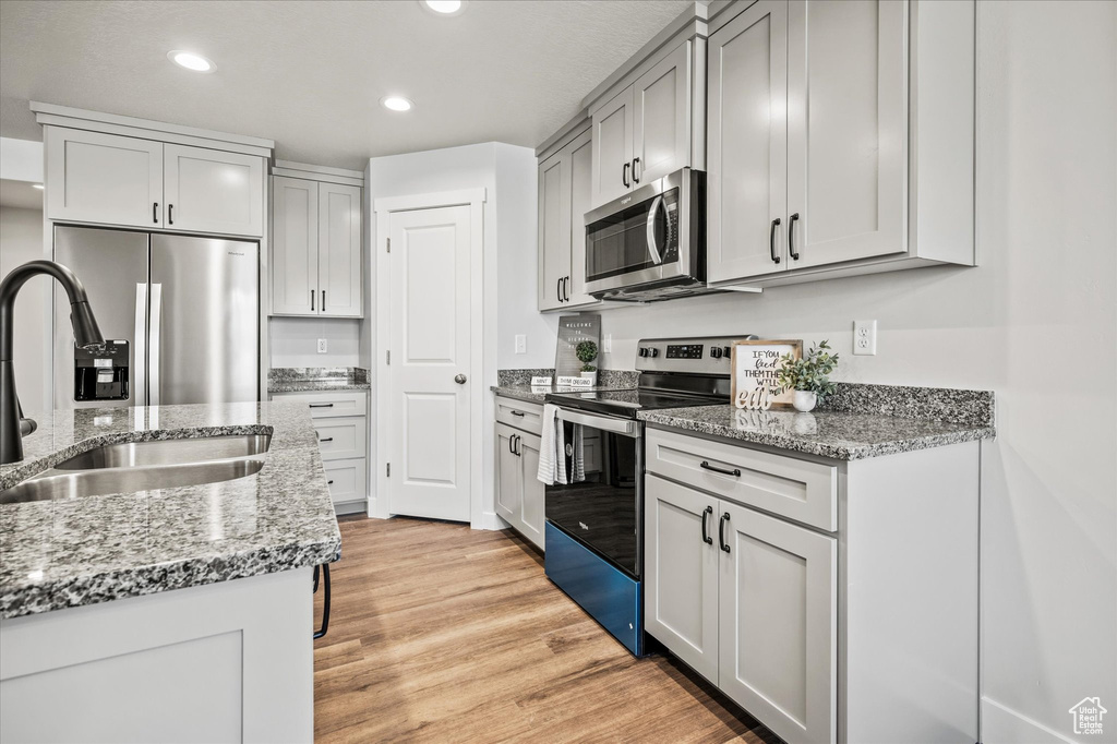 Kitchen featuring light stone countertops, sink, stainless steel appliances, and light hardwood / wood-style flooring