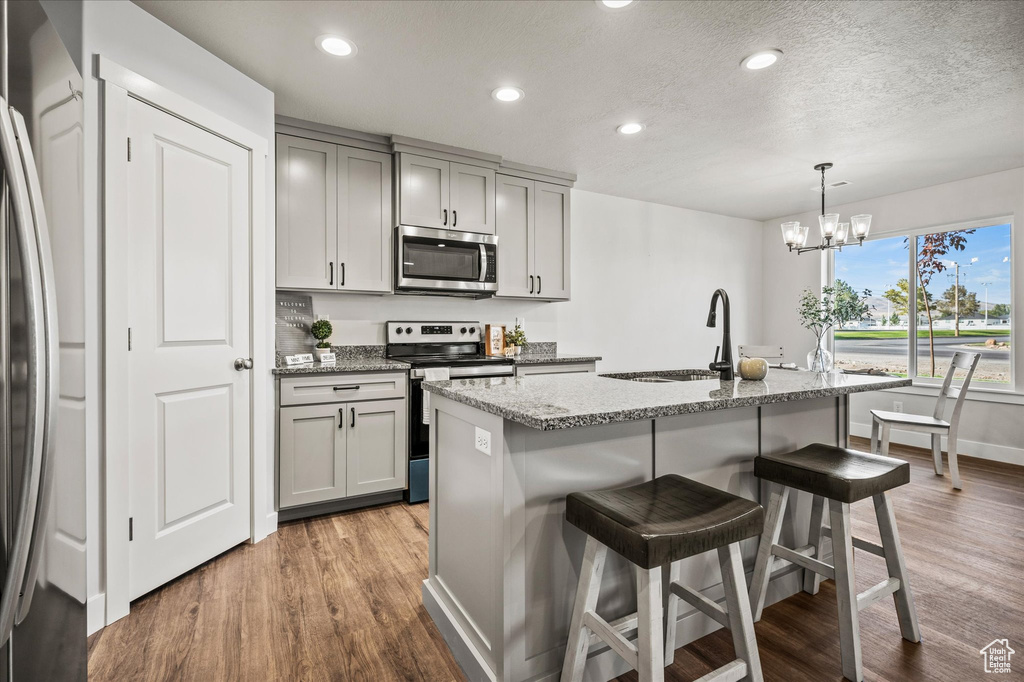 Kitchen featuring light stone countertops, gray cabinetry, pendant lighting, appliances with stainless steel finishes, and a center island with sink