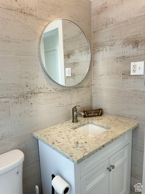 Bathroom featuring toilet, tile walls, and vanity