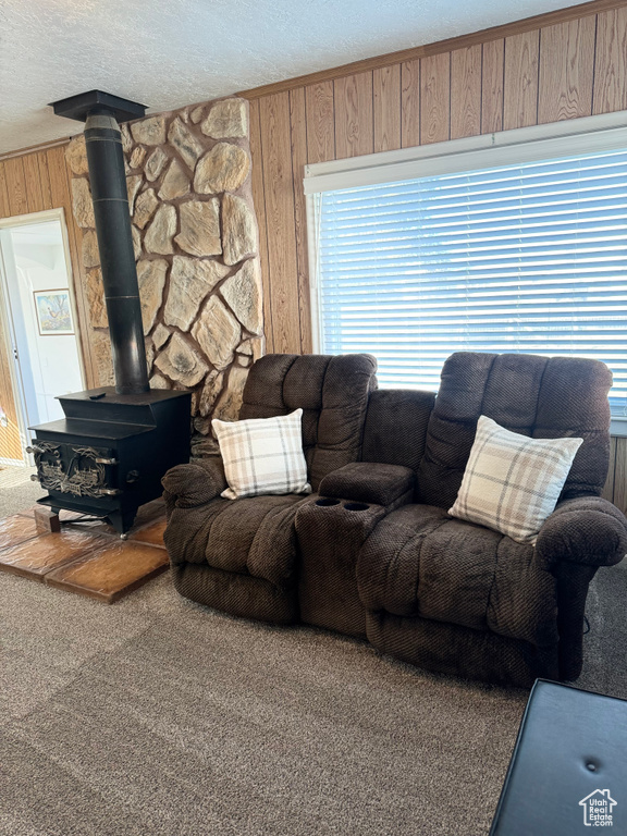 Living room with a wood stove, wooden walls, carpet, and a textured ceiling