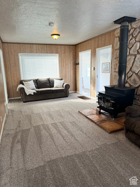 Carpeted living room featuring wood walls, a textured ceiling, and a wood stove