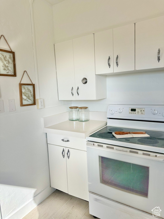 Kitchen with light wood-type flooring, white electric stove, and white cabinetry