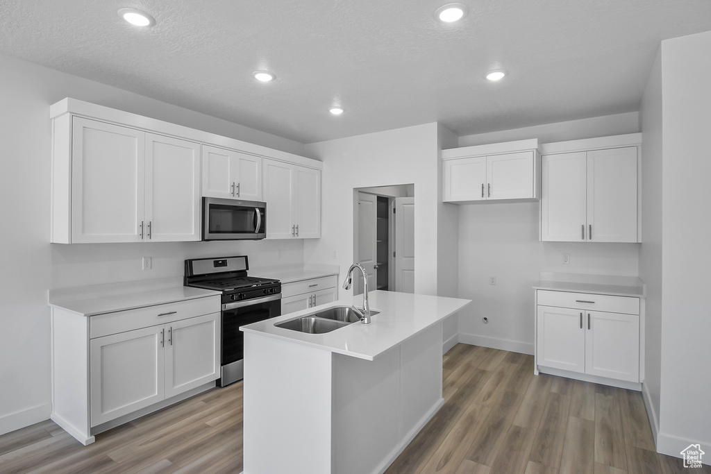 Kitchen with a kitchen island with sink, light wood-type flooring, sink, stainless steel appliances, and white cabinets