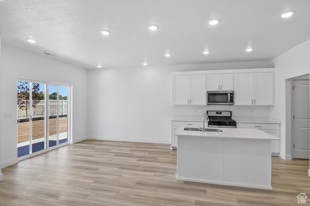 Kitchen featuring light hardwood / wood-style flooring, sink, stainless steel appliances, an island with sink, and white cabinetry