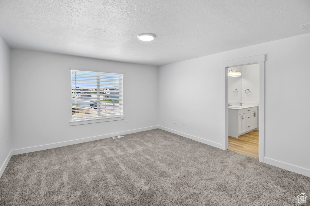 Unfurnished bedroom with light colored carpet, a textured ceiling, and ensuite bathroom