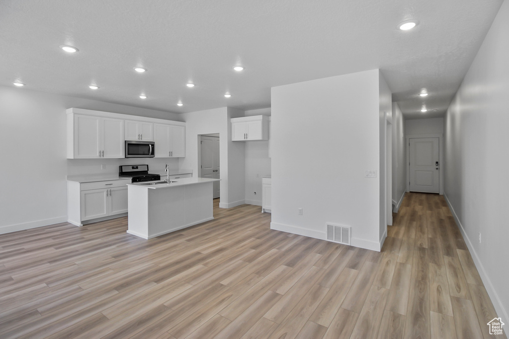 Kitchen featuring an island with sink, sink, light hardwood / wood-style flooring, white cabinetry, and stainless steel appliances