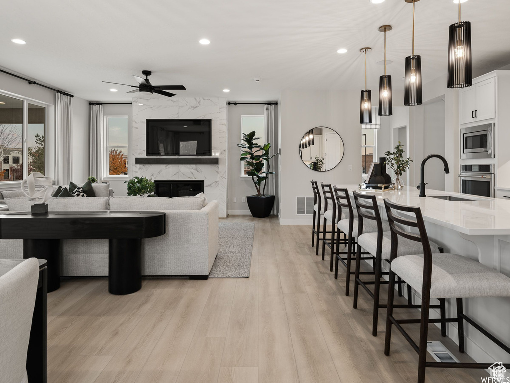 Living room with light hardwood / wood-style flooring, a high end fireplace, sink, and ceiling fan