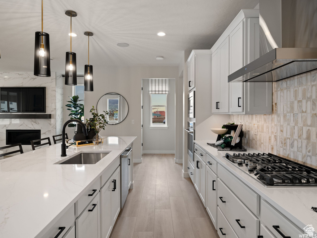 Kitchen with sink, wall chimney exhaust hood, white cabinetry, stainless steel appliances, and light hardwood / wood-style floors