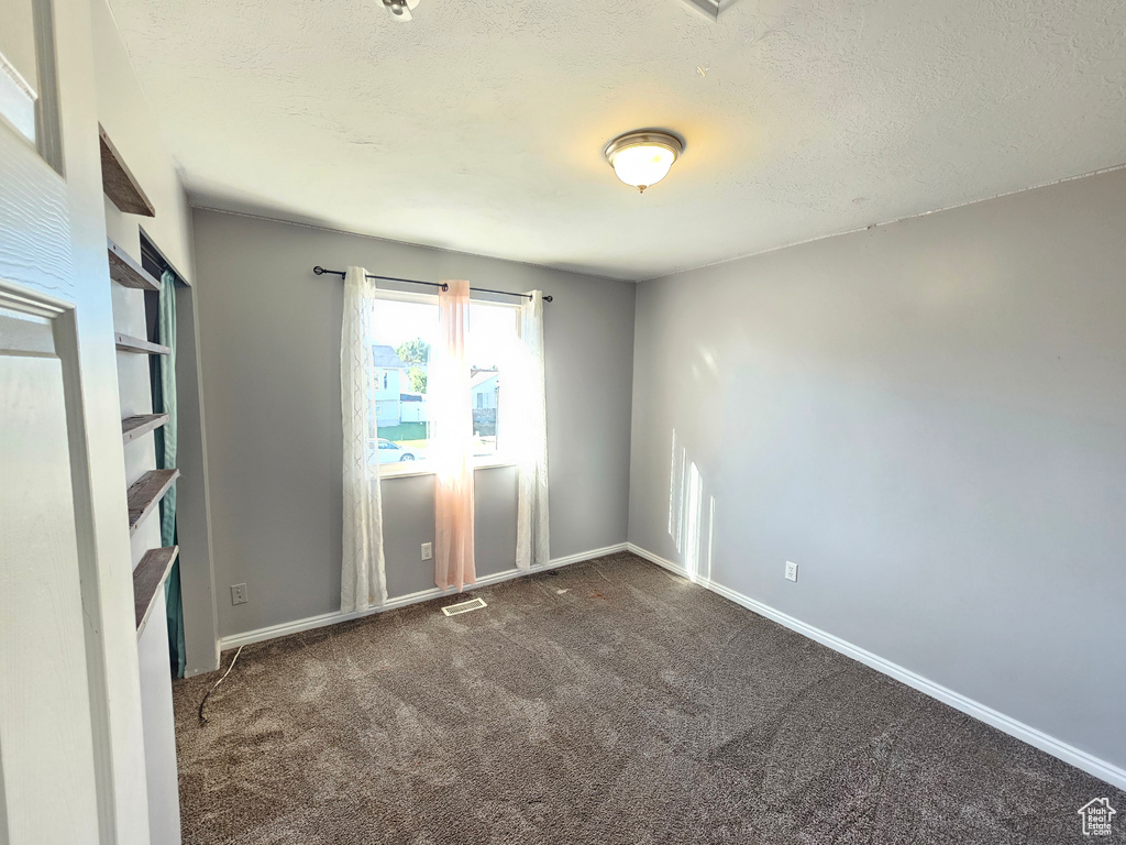 Spare room featuring dark carpet and a textured ceiling