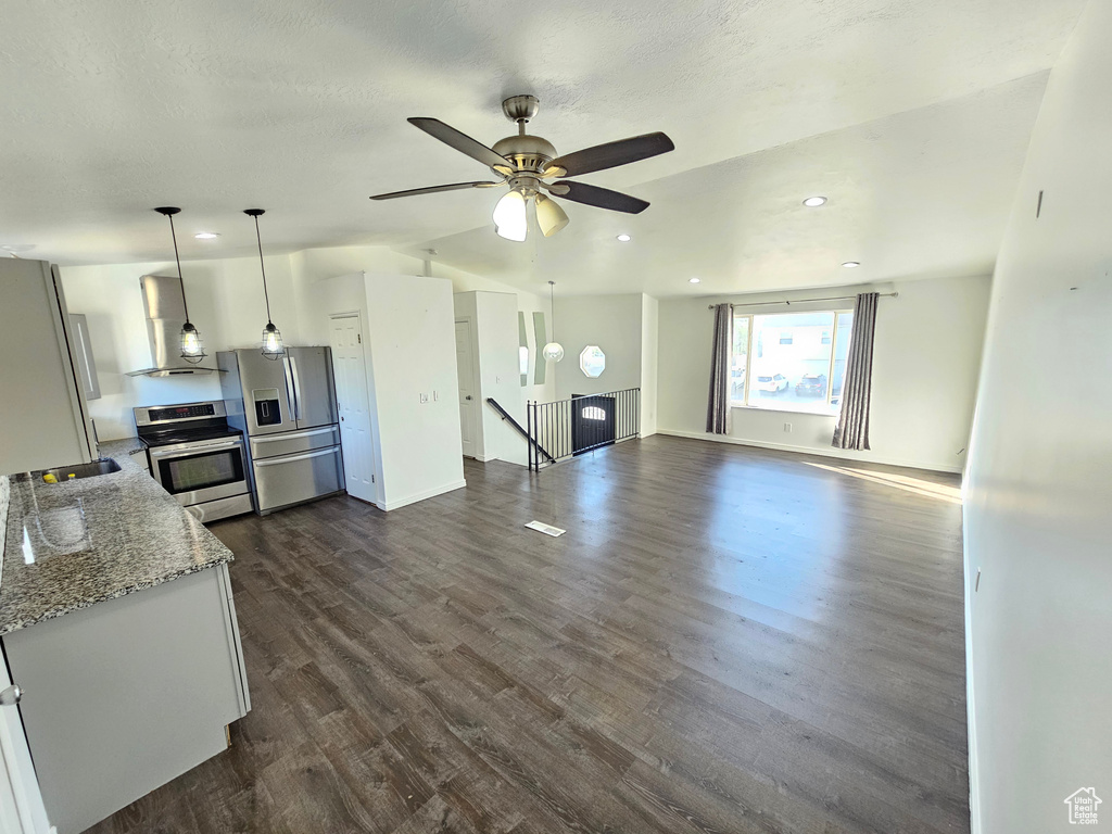 Kitchen featuring pendant lighting, dark wood-type flooring, light stone counters, stainless steel appliances, and exhaust hood