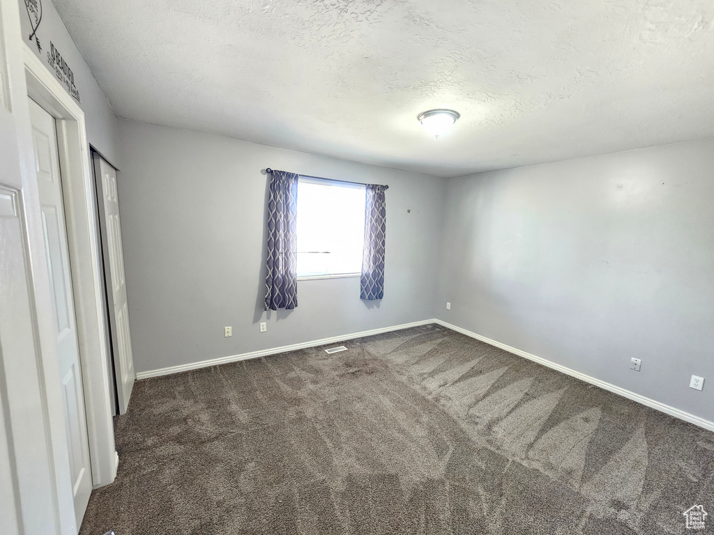 Unfurnished bedroom featuring dark colored carpet and a textured ceiling