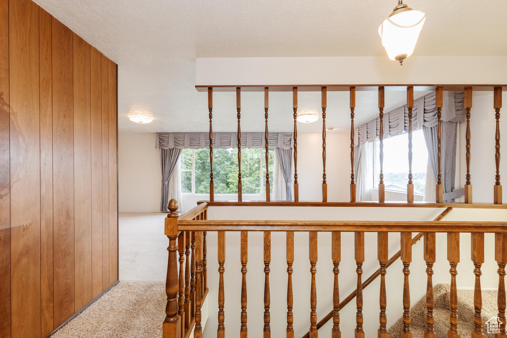 Stairs featuring carpet floors, wooden walls, and a textured ceiling