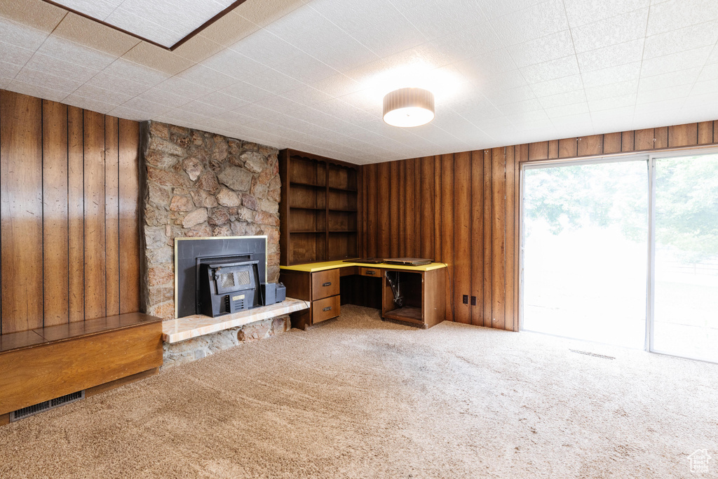 Unfurnished living room featuring wood walls, a wood stove, and carpet