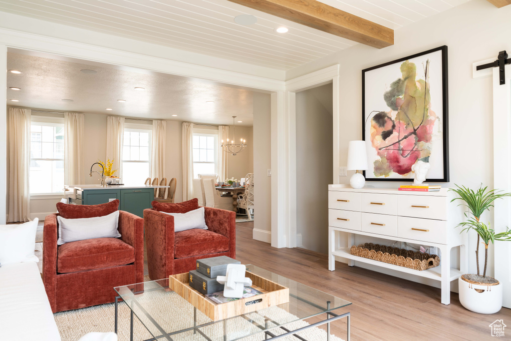 Living room with beamed ceiling, a barn door, an inviting chandelier, and light hardwood / wood-style flooring