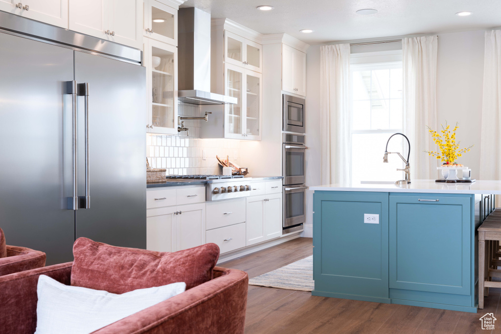 Kitchen featuring white cabinets, tasteful backsplash, wall chimney exhaust hood, built in appliances, and dark hardwood / wood-style flooring