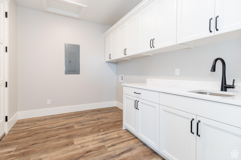 Clothes washing area with electric panel, cabinets, light wood-type flooring, hookup for a washing machine, and sink