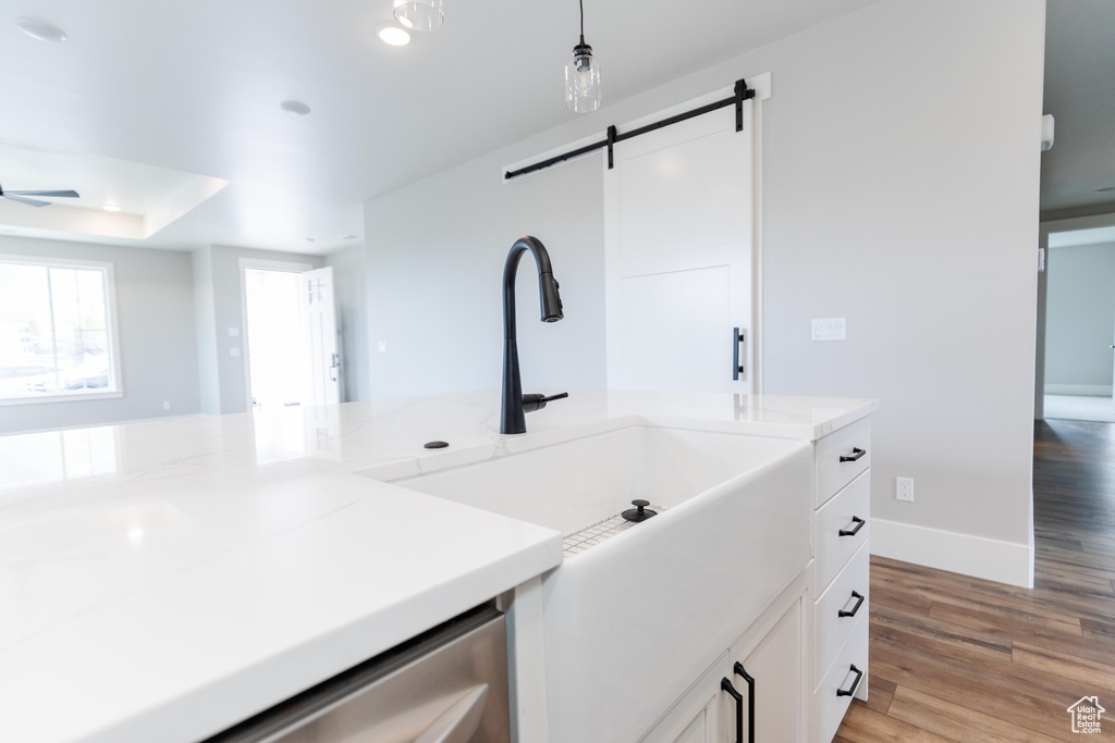 Interior space featuring a barn door, ceiling fan, pendant lighting, light hardwood / wood-style flooring, and white cabinetry