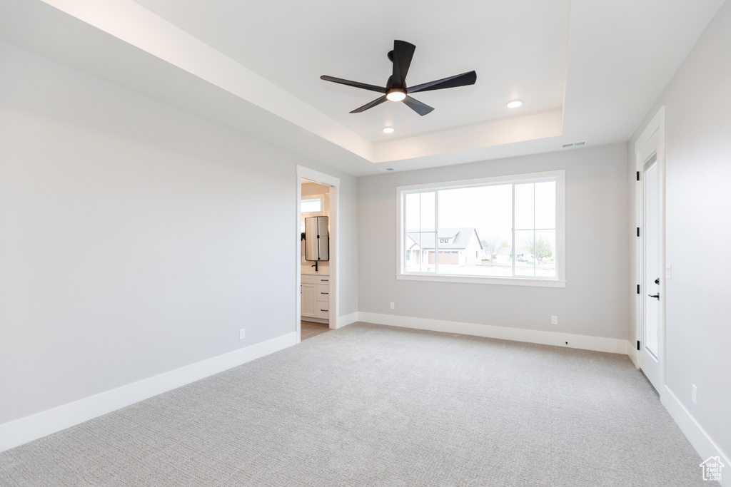 Unfurnished bedroom featuring light carpet, a raised ceiling, connected bathroom, and ceiling fan