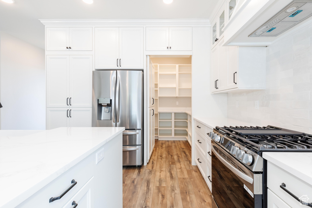 Kitchen featuring white cabinets, appliances with stainless steel finishes, light hardwood / wood-style flooring, and exhaust hood