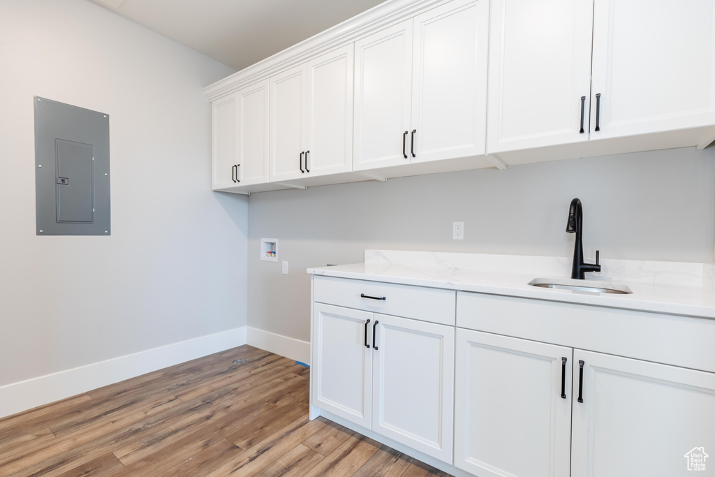 Laundry area with washer hookup, electric panel, cabinets, light wood-type flooring, and sink