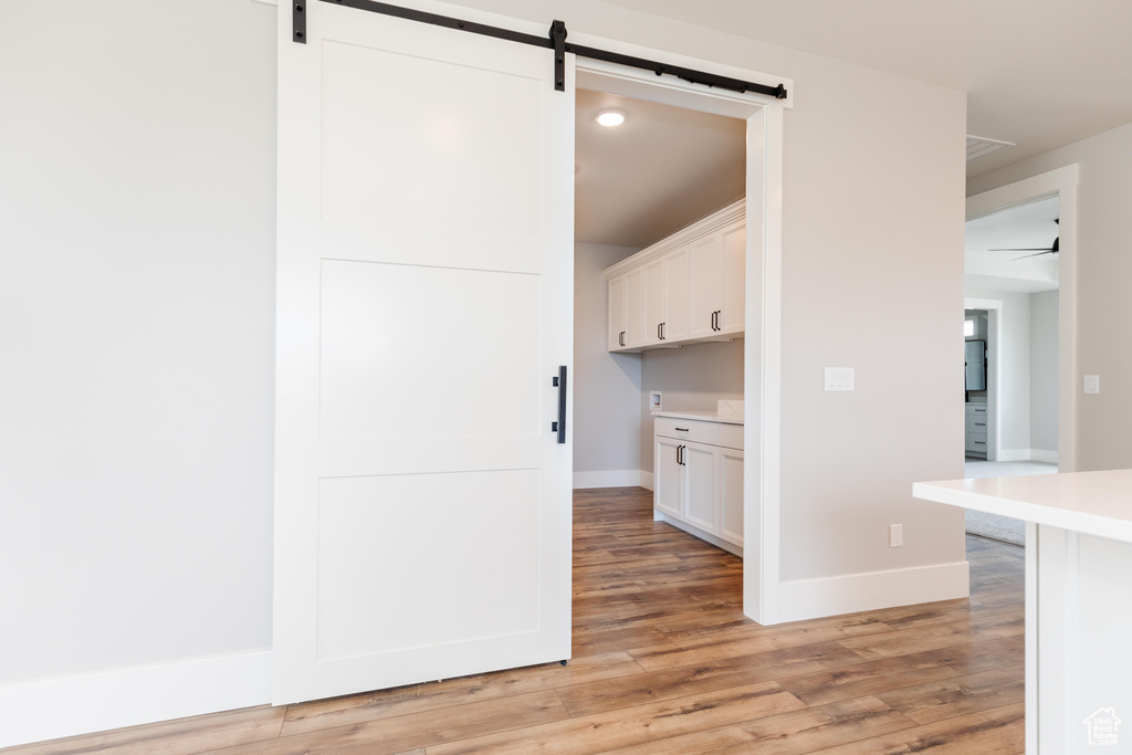 Interior space with ceiling fan, white cabinets, light wood-type flooring, and a barn door