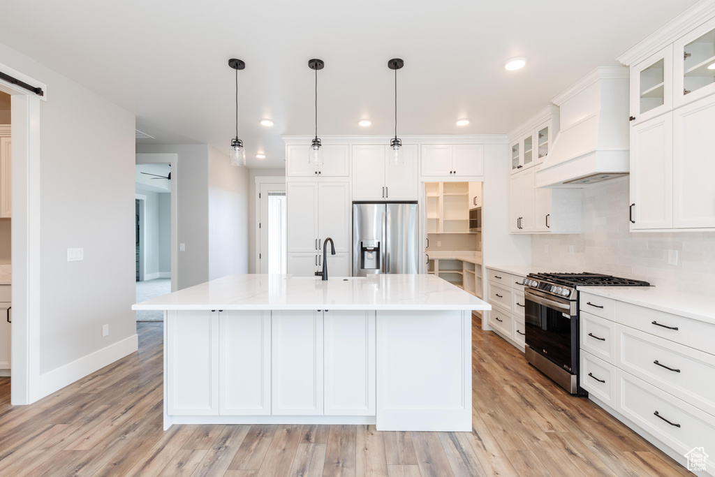 Kitchen featuring decorative light fixtures, a kitchen island with sink, stainless steel appliances, light wood-type flooring, and a barn door