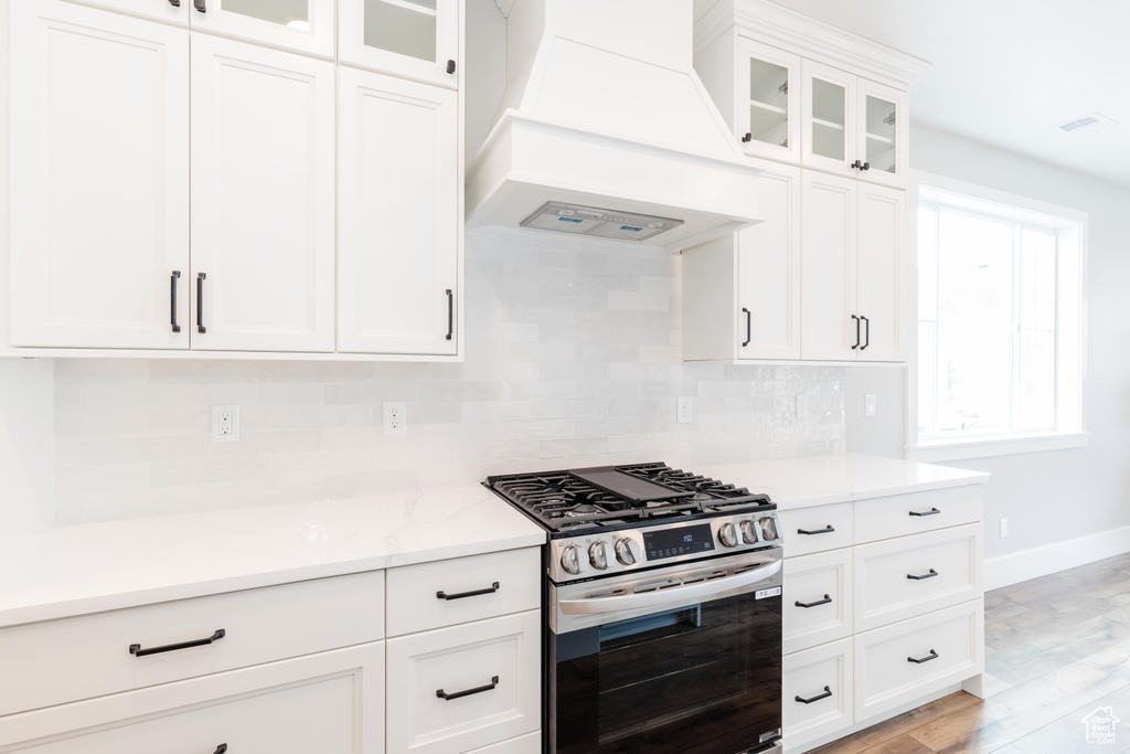 Kitchen featuring light hardwood / wood-style floors, decorative backsplash, custom range hood, stainless steel gas stove, and white cabinetry