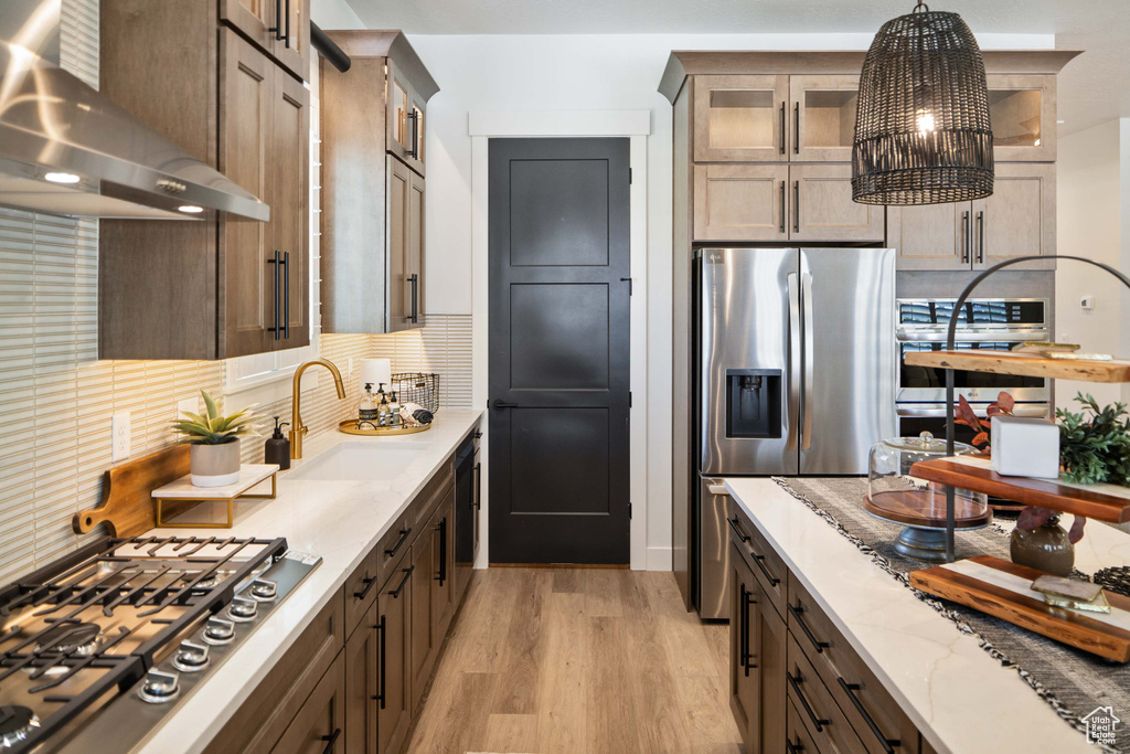 Kitchen featuring exhaust hood, sink, light hardwood / wood-style floors, an inviting chandelier, and decorative light fixtures