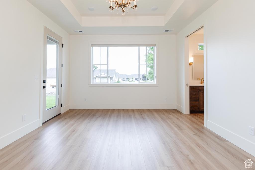 Spare room featuring an inviting chandelier, a raised ceiling, and light hardwood / wood-style flooring