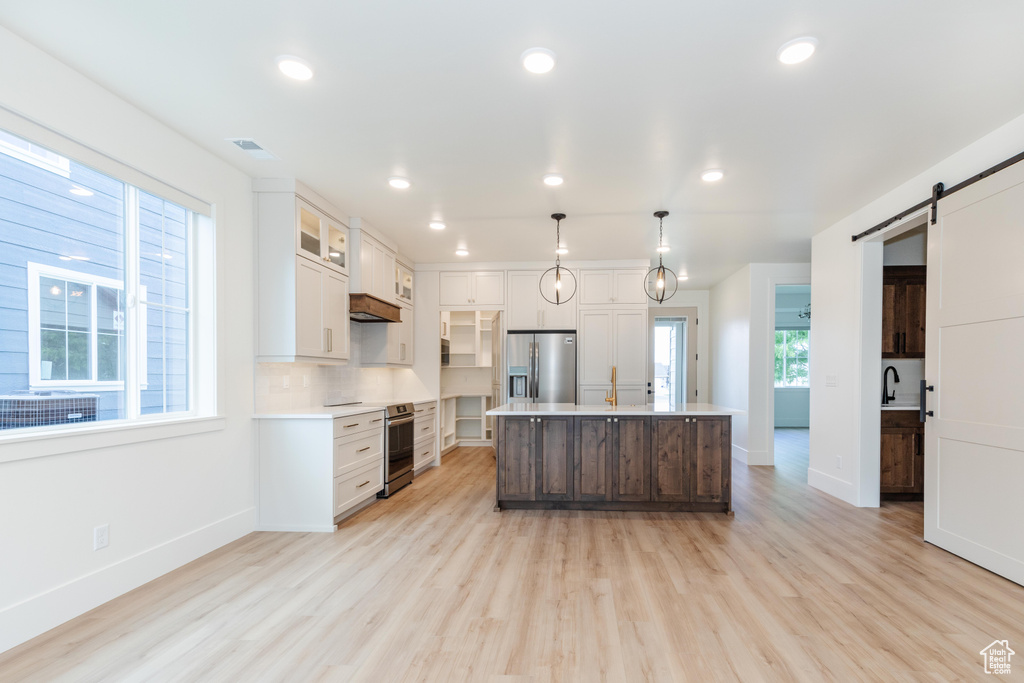 Kitchen featuring an island with sink, pendant lighting, stainless steel appliances, and light hardwood / wood-style flooring