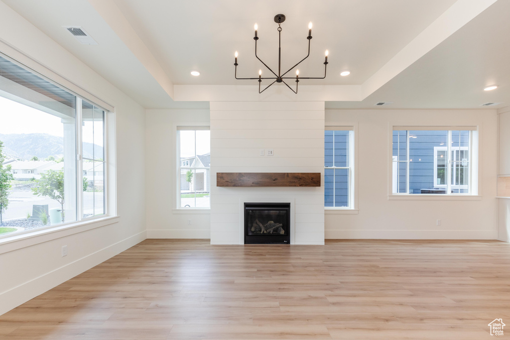 Unfurnished living room with a raised ceiling, a chandelier, light hardwood / wood-style flooring, and a mountain view