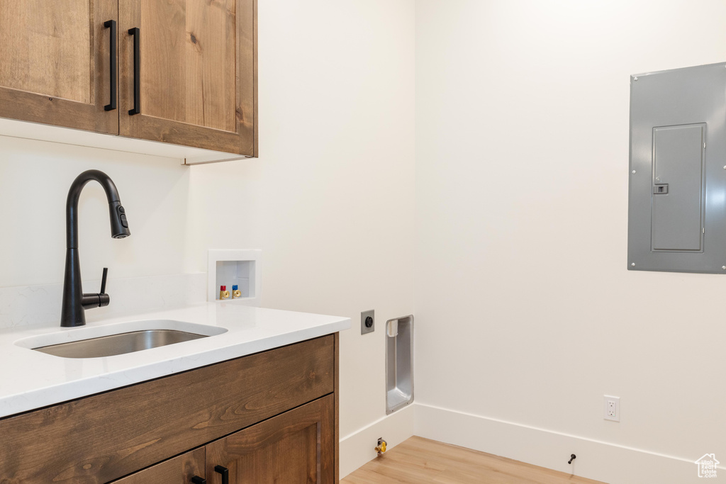 Laundry room with washer hookup, electric panel, cabinets, light hardwood / wood-style flooring, and sink