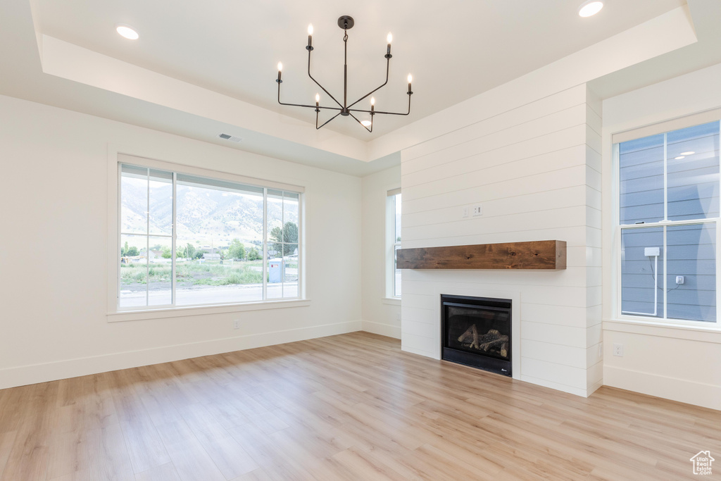 Unfurnished living room featuring light wood-type flooring, an inviting chandelier, and a raised ceiling