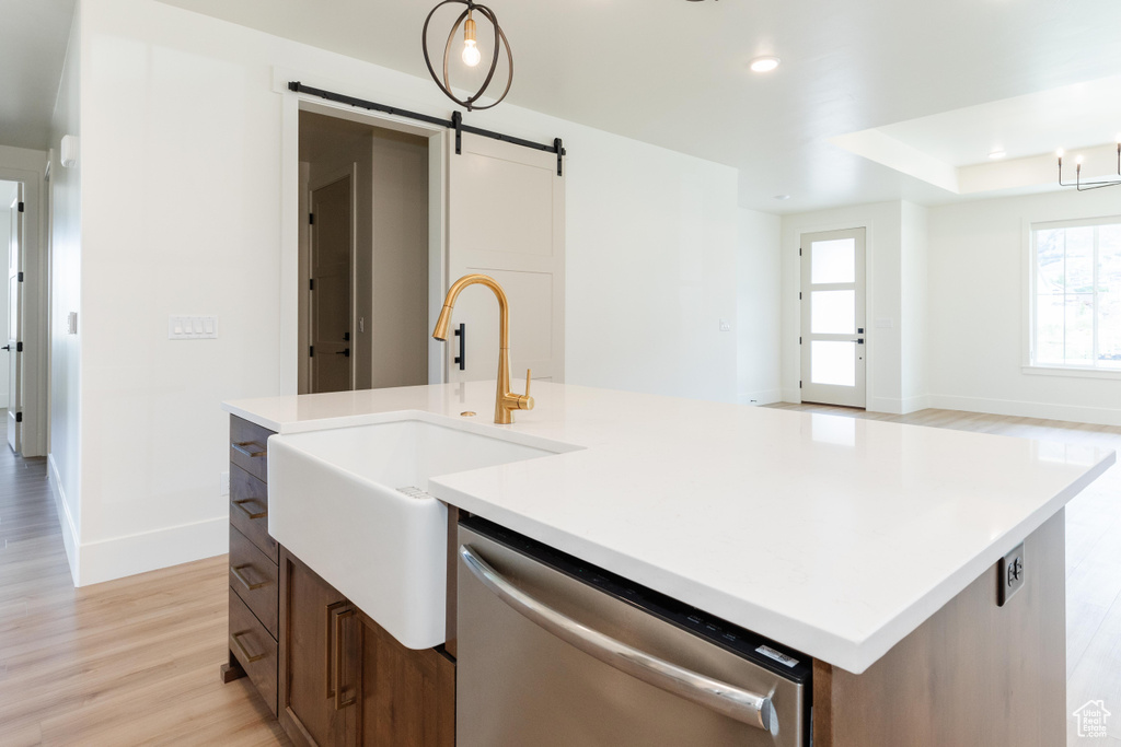 Kitchen featuring an island with sink, a barn door, stainless steel dishwasher, and light hardwood / wood-style floors