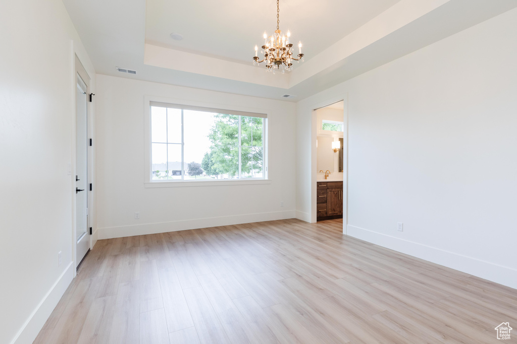 Unfurnished bedroom with a raised ceiling, light hardwood / wood-style floors, an inviting chandelier, and ensuite bath